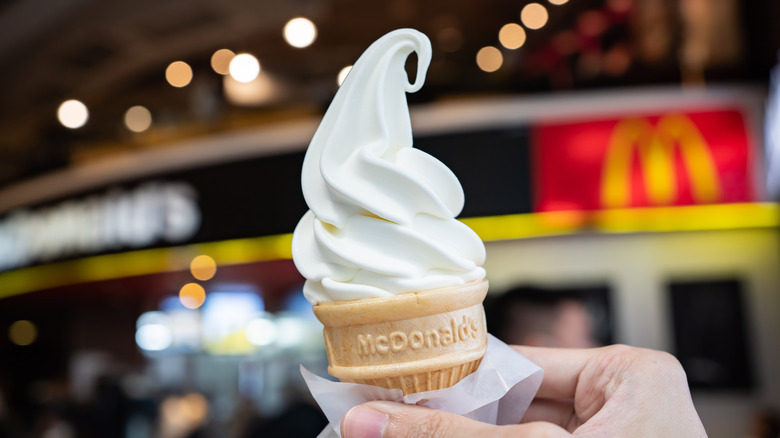 A hand holding a McDonald's vanilla soft serve cone