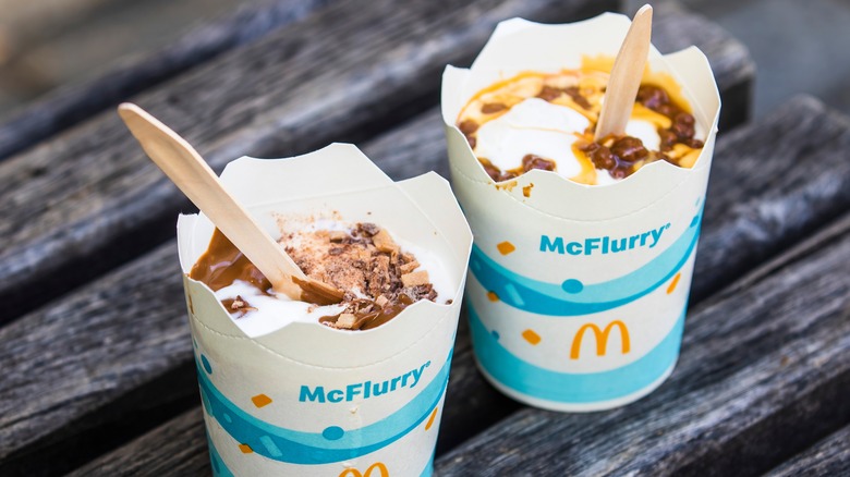 Two McDonald's McFlurries in paper cups with wooden spoons and chocolate toppings