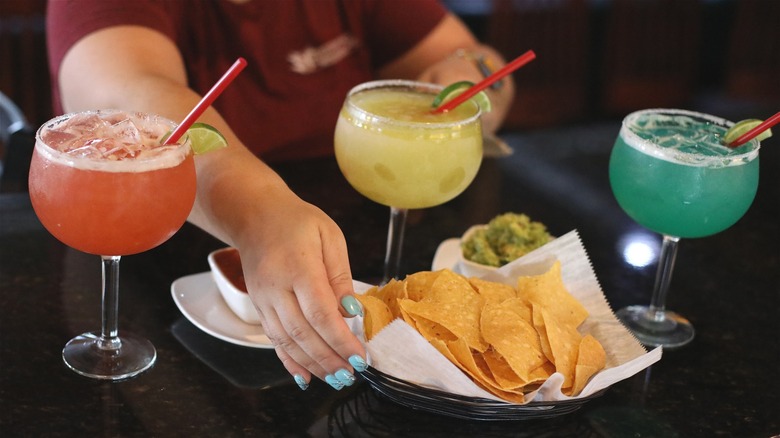 hand reaching for tortilla chips on a table with colorful margarita cocktails