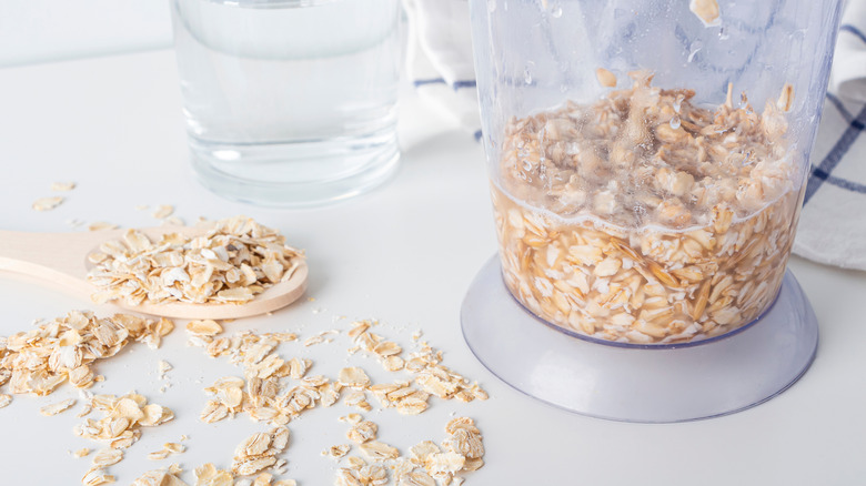 Oats rest on the countertop and spoon, with some combined with water in a blender