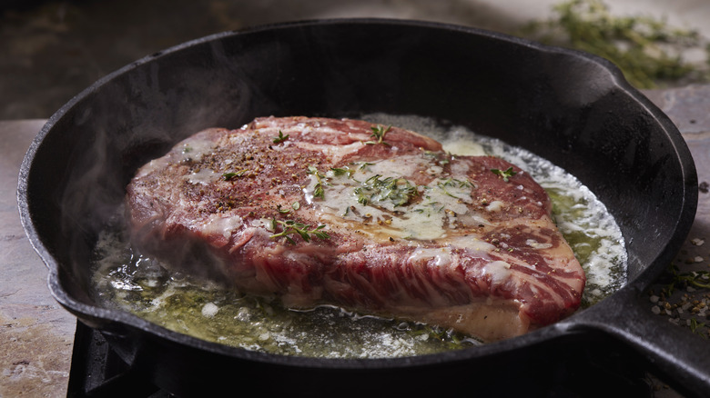 large piece of steak searing in pan