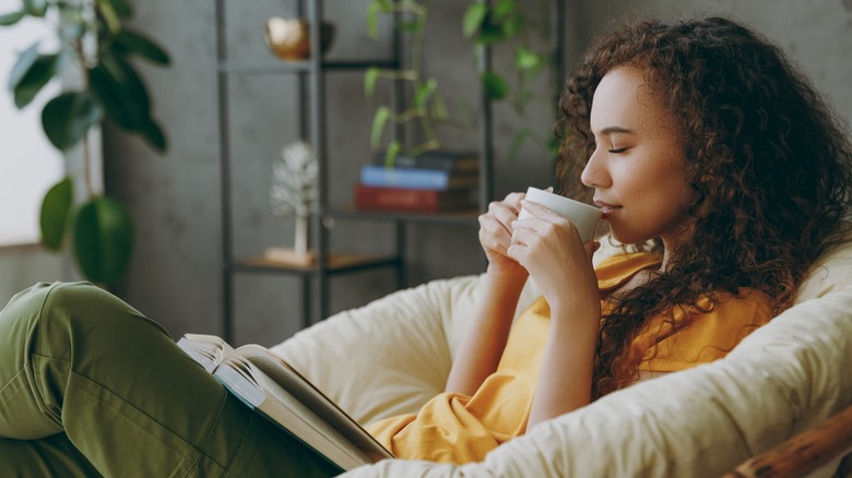 person relaxing with a book and holding a mug to their mouth