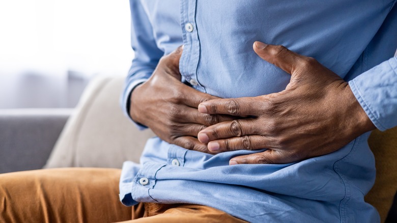 A man in a blue button-down holds his stomach because it's upset