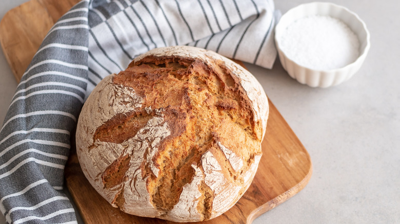 round loaf of bread on wooden cutting board next to bowl of salt