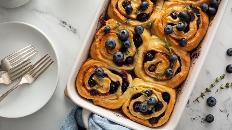 Pan of cinnamon rolls with blueberries and thyme sprigs
