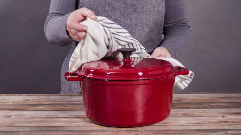 Person handles red dutch oven with towel