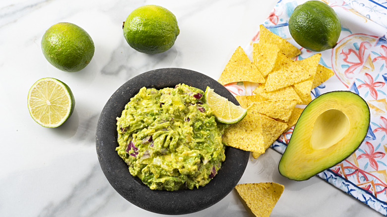 A bowl of homemade guacamole next to lime and tortilla chips