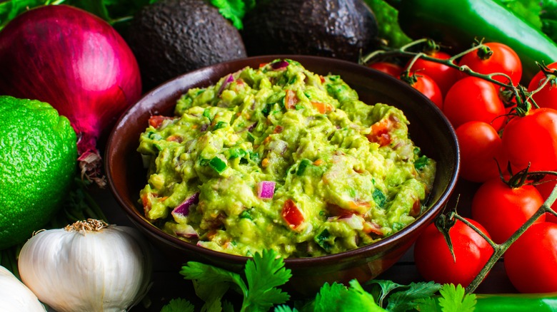 A bowl of chunky guacamole surrounded by various ingredients