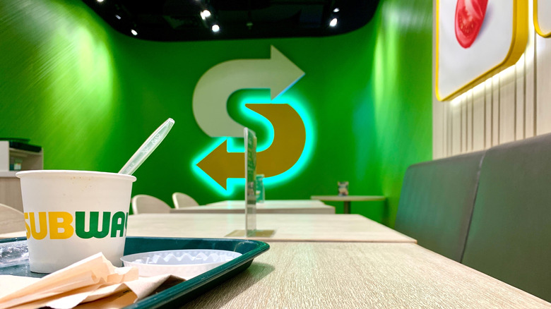 Green restaurant wall with Subway logo and a table with a Subway branded cup on the table