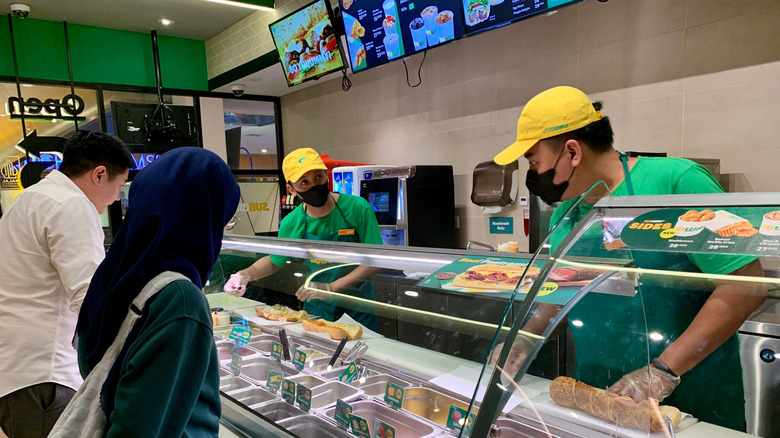 Subway employees preparing a sub for two customers