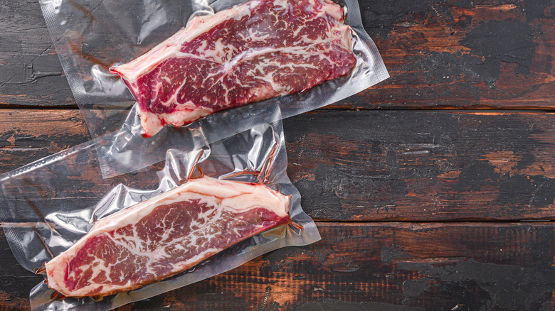 Two raw steaks in a vacuum sealed package on a wooden table