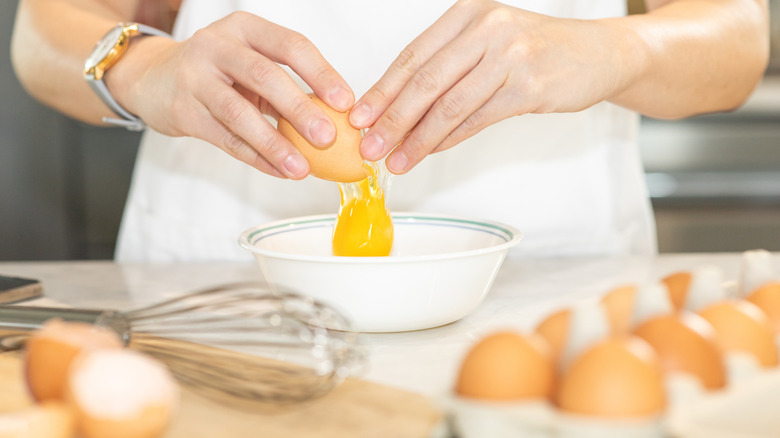 Hands crack a chicken egg into a white bowl