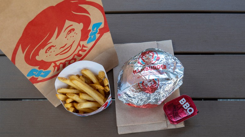 A Wendy's meal with french fries, hamburger, and BBQ sauce sit on a wood table