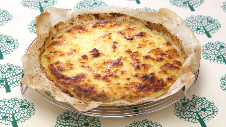 A full wheel of bread cheese wrapped in parchment paper on a floral tablecloth