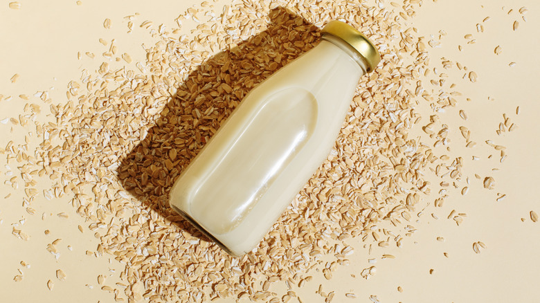 bottle of oat milk sitting on top of scattered oats