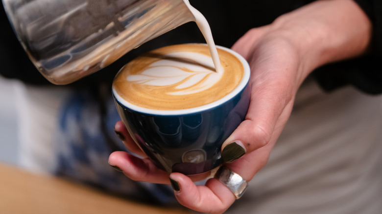 barista pouring oatmilk into a creamy coffee