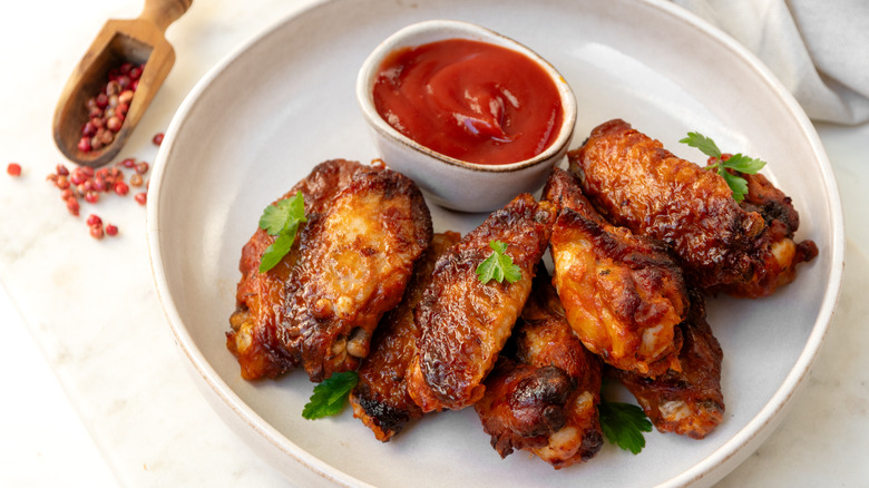 A plate of chicken wings and sauce on a white table