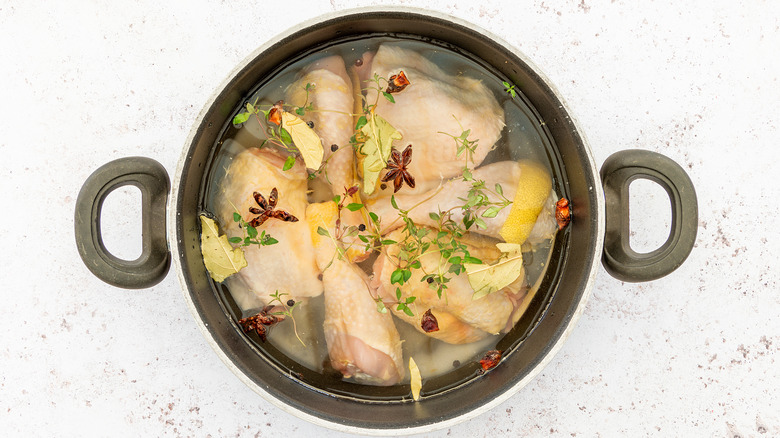 Cooking pot full of raw chicken in a wet brine with spices and herbs