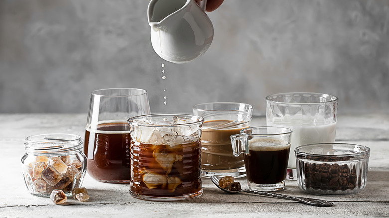 Person pouring milk into iced coffee