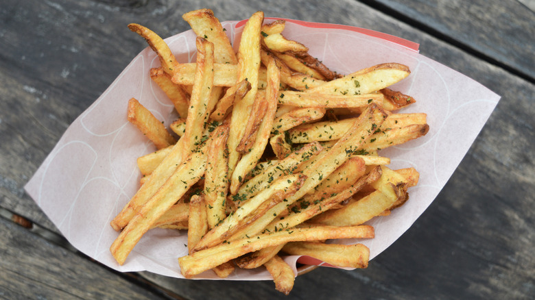 A portion of french fries sit in paper on a wooden table.