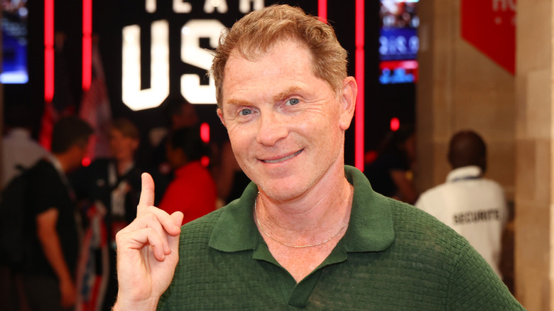 Bobby Flay smiling in front of Team USA sign