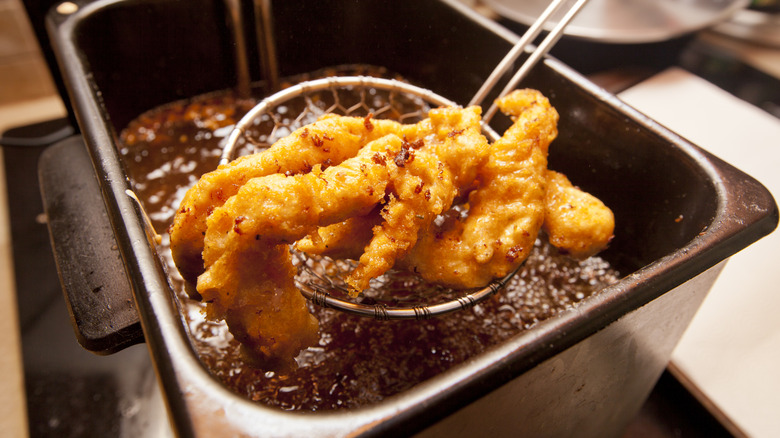 Fried chicken being scooped out of a tabletop deep fryer