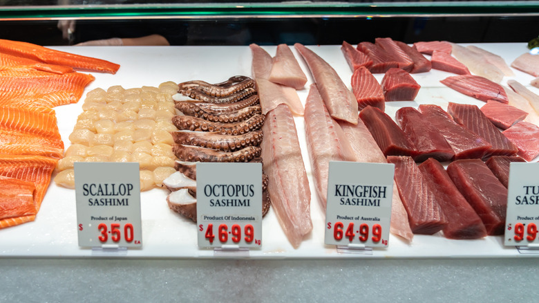 Display of raw scallops, tuna, and more seafood in display case with price tags