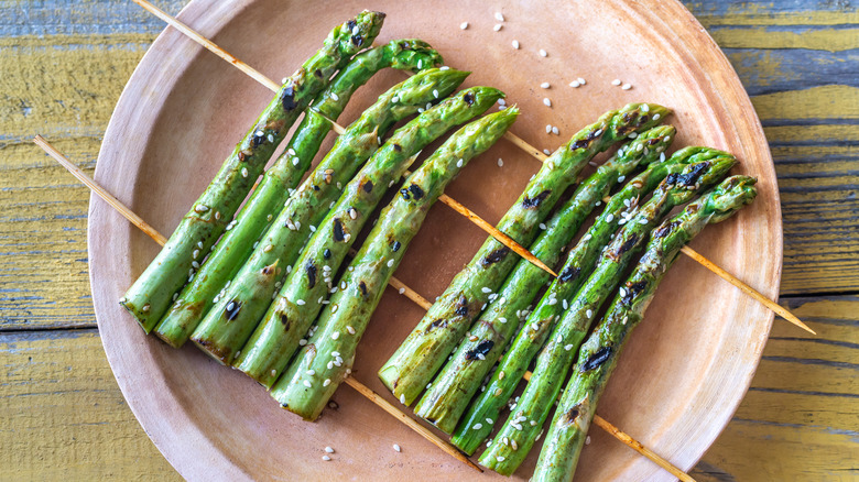 Two rafts of skewered grilled asparagus on a pink plate