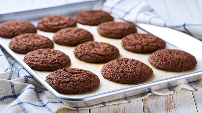 a tray of chocolate cookies on a towel, resting on a white wooden surface