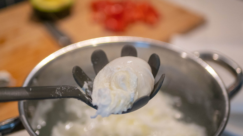 Poached egg being removed from water with slotted spoon