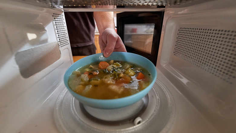 man taking soup out of the microwave