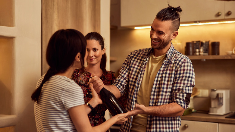 A smiling dinner party guest hands a bottle of wine to a host