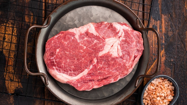 large piece of prime rib steak on metal tray next to dish of pink salt