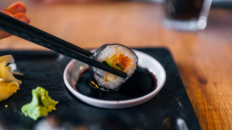 Sushi being dunked into soy sauce with chopsticks