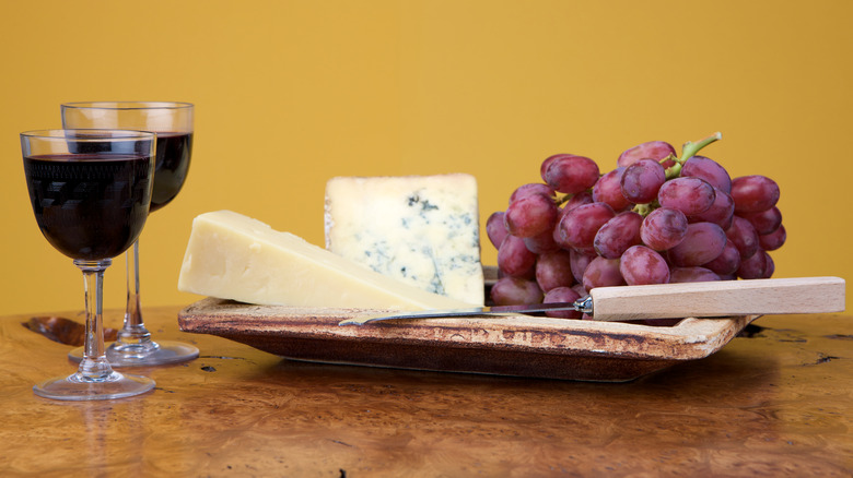 Stilton and cheddar cheese on a board with grapes and glasses of port