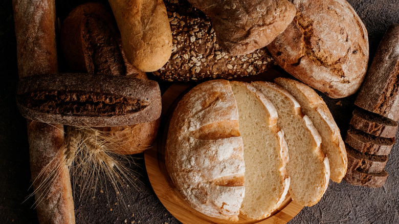 A variety of homemade, rustic bread loaves sit on a table next to sprigs of wheat