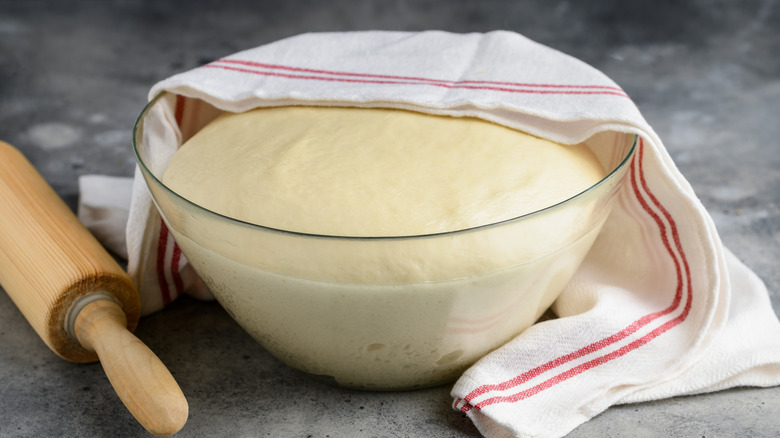 Bread dough proofing in a glass bowl covered by a white and red towel