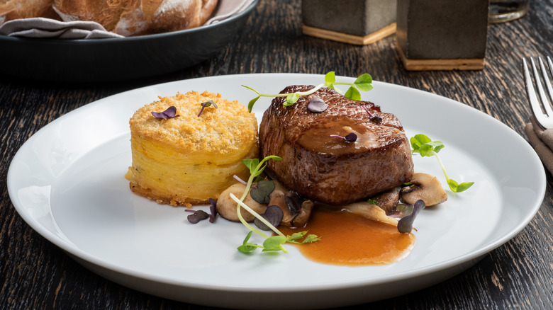 Steak with a glossy dark crust with side of potato, mushrooms, and microgreens