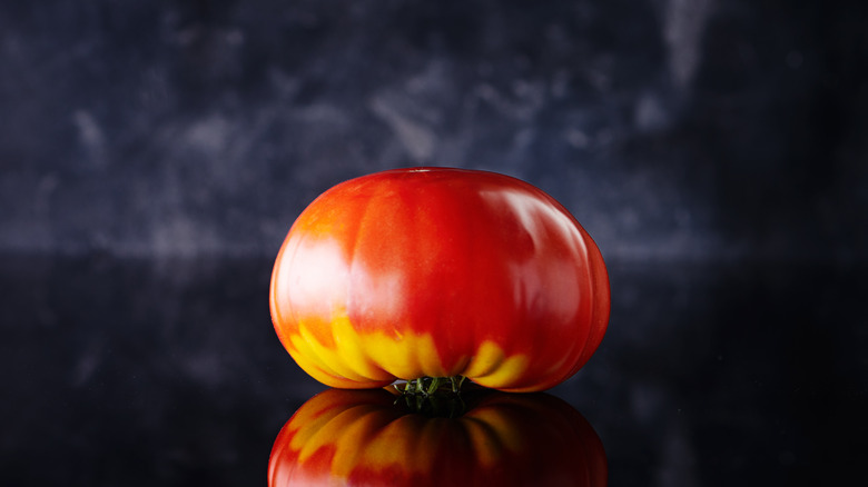 Single whole tomato sitting upside down on black reflective surface