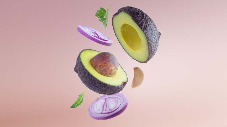 Cut avocado halves with slices of red onion, garlic cloves, and cilantro leaves thrown into the air