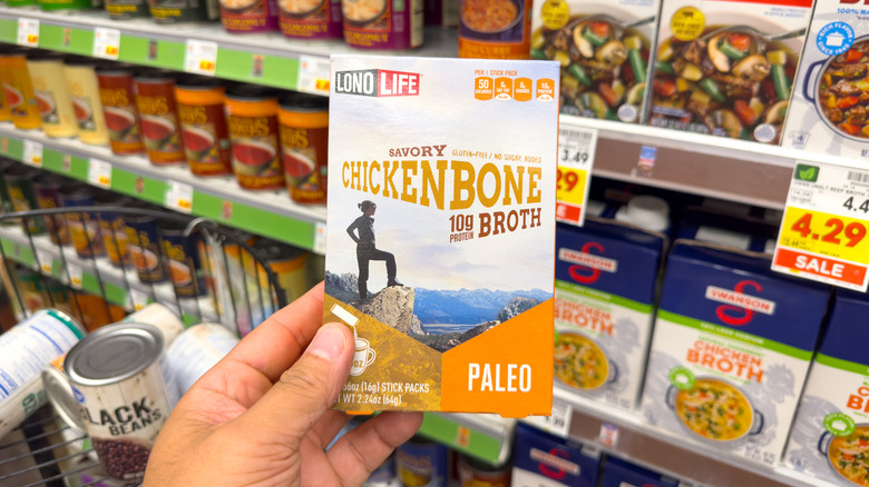 A hand holds a box of chicken bone broth in a grocery store aisle