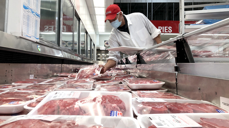 A Costco employee stacks steaks in a display case.