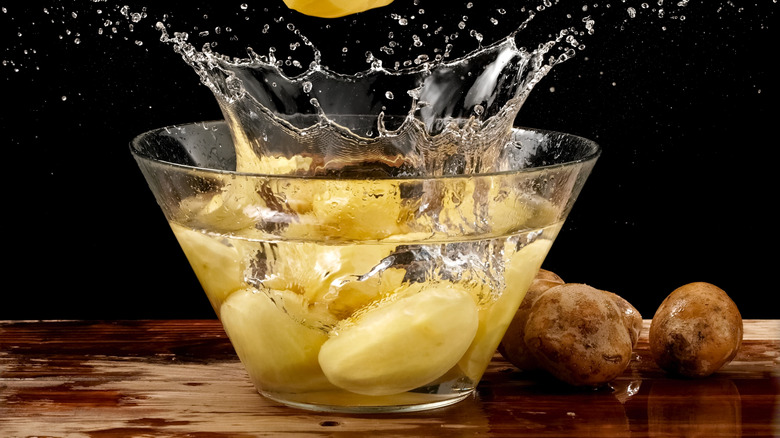 Potatoes splashing into a glass bowl of water