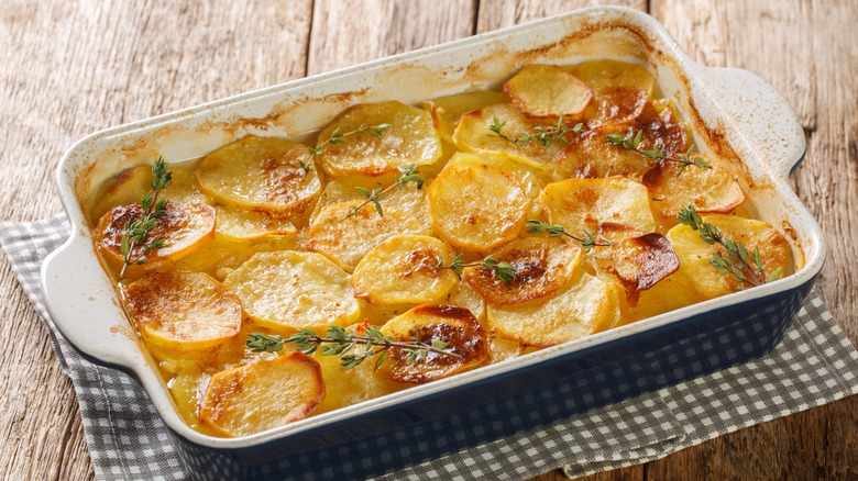 A pan with scalloped potatoes and a thyme garnish