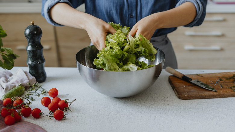 A chef mixes salad greens in a silver bowl using their hands