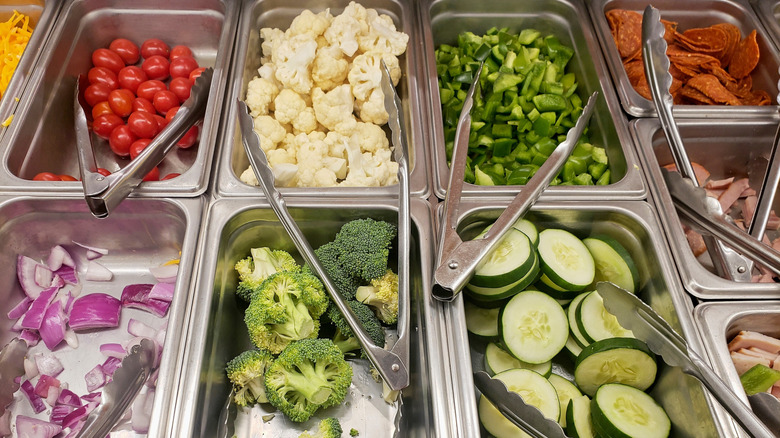 A variety of vegetables are separated into refrigerated bins at a salad bar.