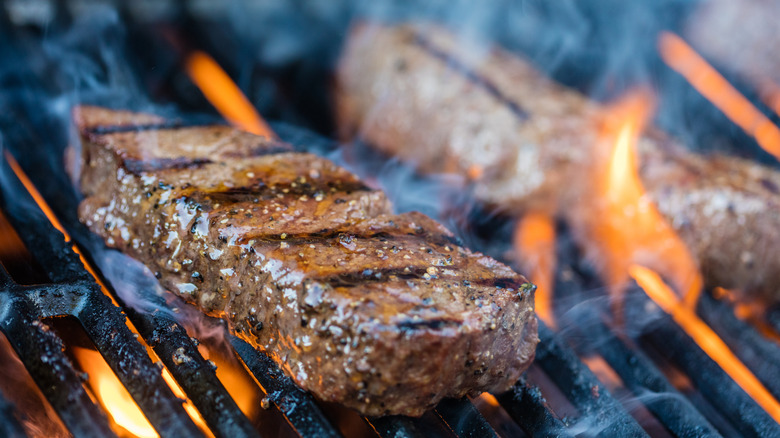 A cut of steak sits on a hot grill surrounded by flames