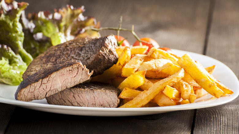 A well-done steak with no pink interior sits on a plate next to french fries