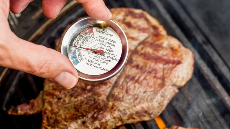 A chef places a meat thermometer that reads 160 degrees Fahrenheit into a cut of steak