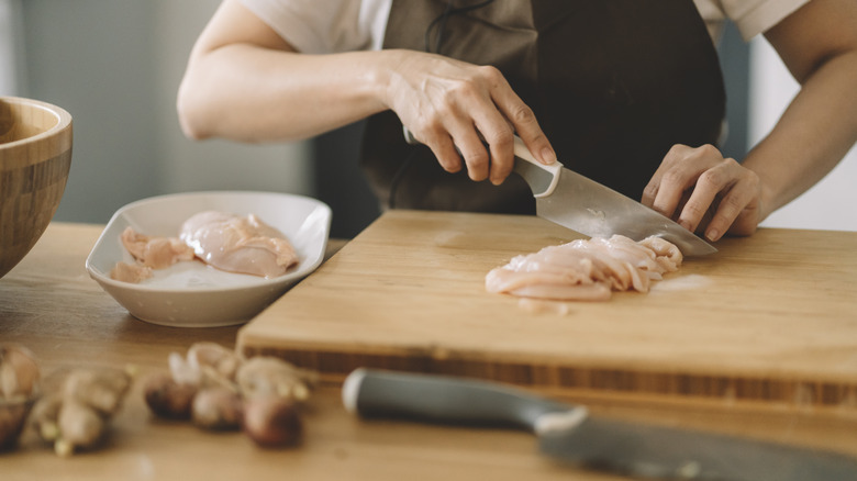 person cutting chicken in board and container